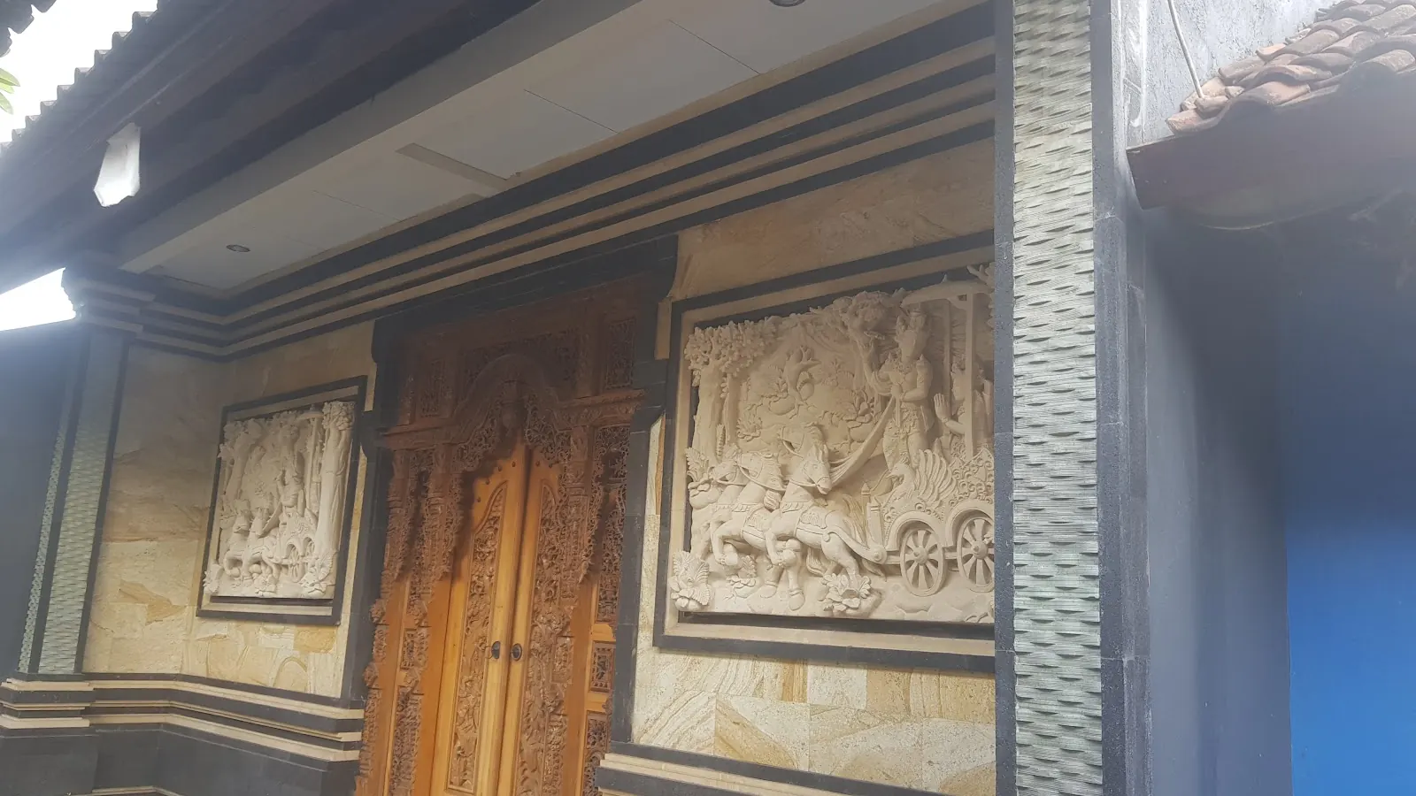 Balinese house front with carved timber doors and stone relief panels
