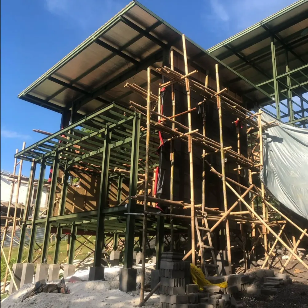 Two-level steel frame building with bamboo scaffolding under a blue sky